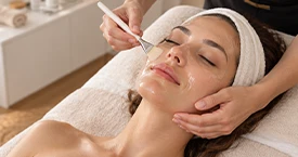 Application d'un soin hydratant au pinceau sur le visage d'une cliente dans un institut de beauté à Lausanne.